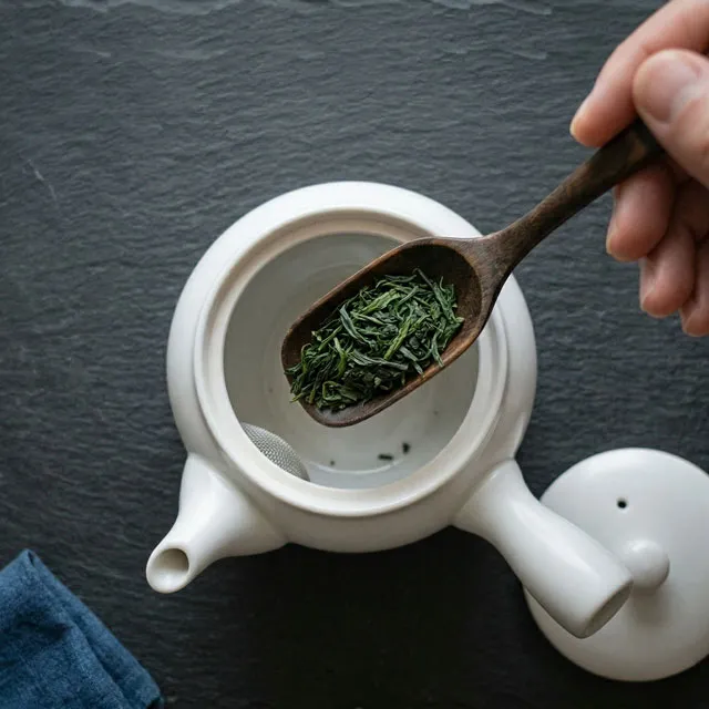 木製の茶さじで計量された新鮮な緑茶の茶葉